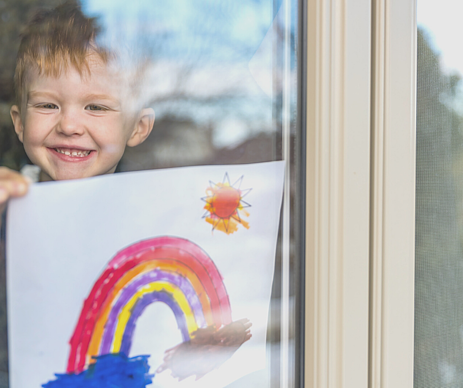 little boy holding rainbow drawing in window